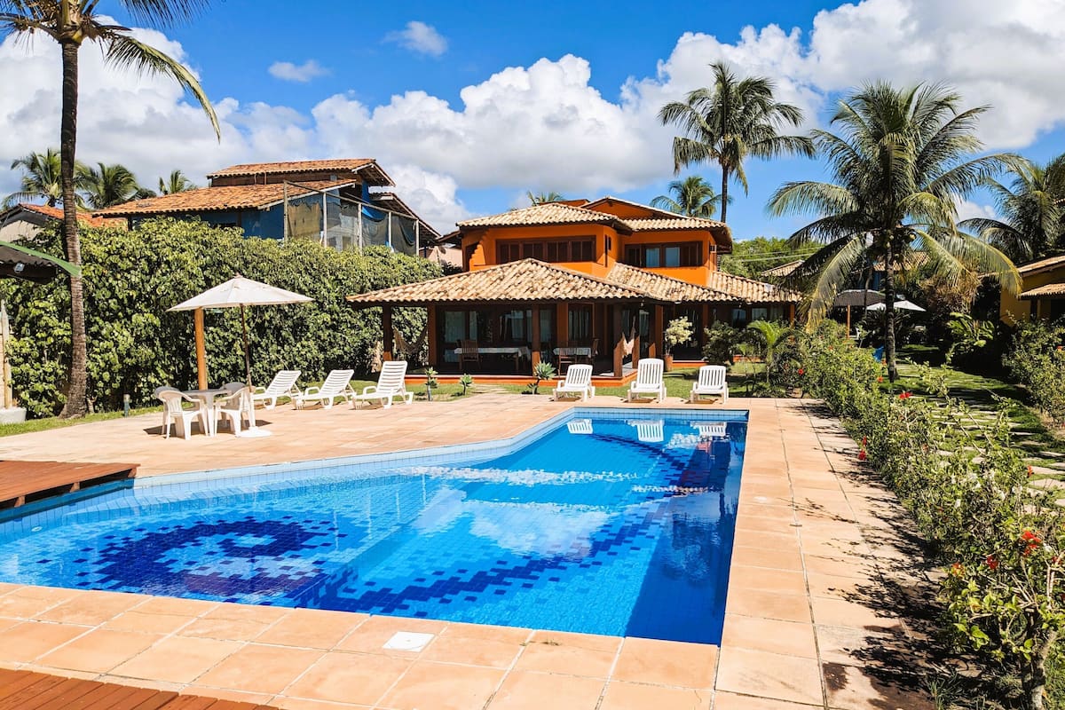 Ein Pool mit Liegestühlen, eine Holzterrasse und ein Haus mit Ziegeldach.