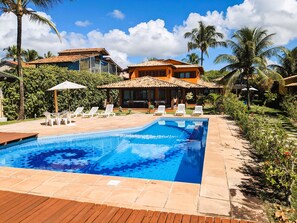 A swimming pool with lounge chairs, a wooden deck, and a house with a tiled roof. - Residence Maria Vittoria (Porto Seguro)