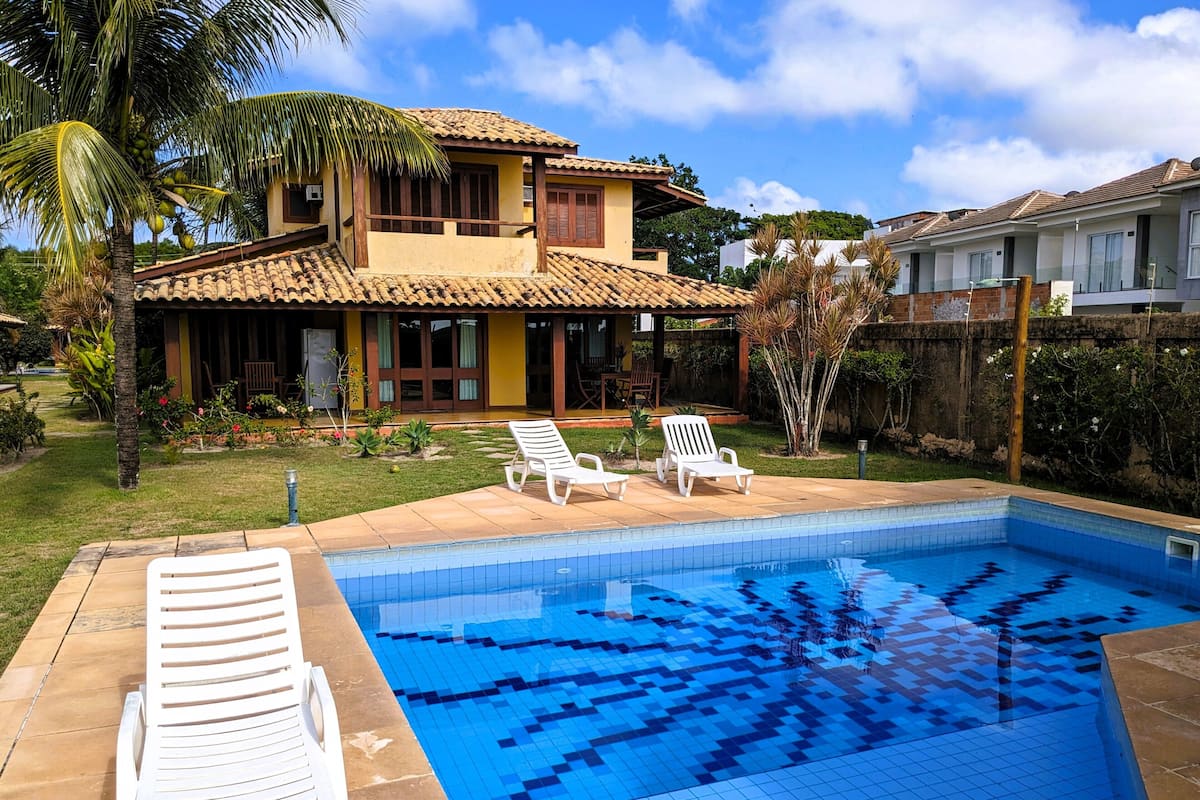 Ein zweistöckiges Haus mit Ziegeldach, einem Swimmingpool und einer Terrasse mit Liegestühlen.
