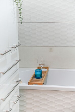A bathroom with white tiled walls, a wooden tray with a blue glass, and a glass on the counter.