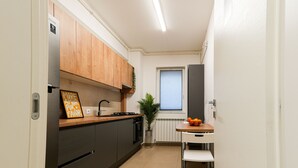 Una cocina moderna con armarios de madera, un refrigerador de acero inoxidable, horno empotrado y un pequeño comedor con una mesa blanca y sillas metálicas.