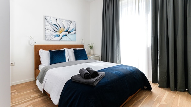 Una cama bien hecha con una colcha azul y blanca, una manta gris y dos toallas enrolladas sobre la cama.