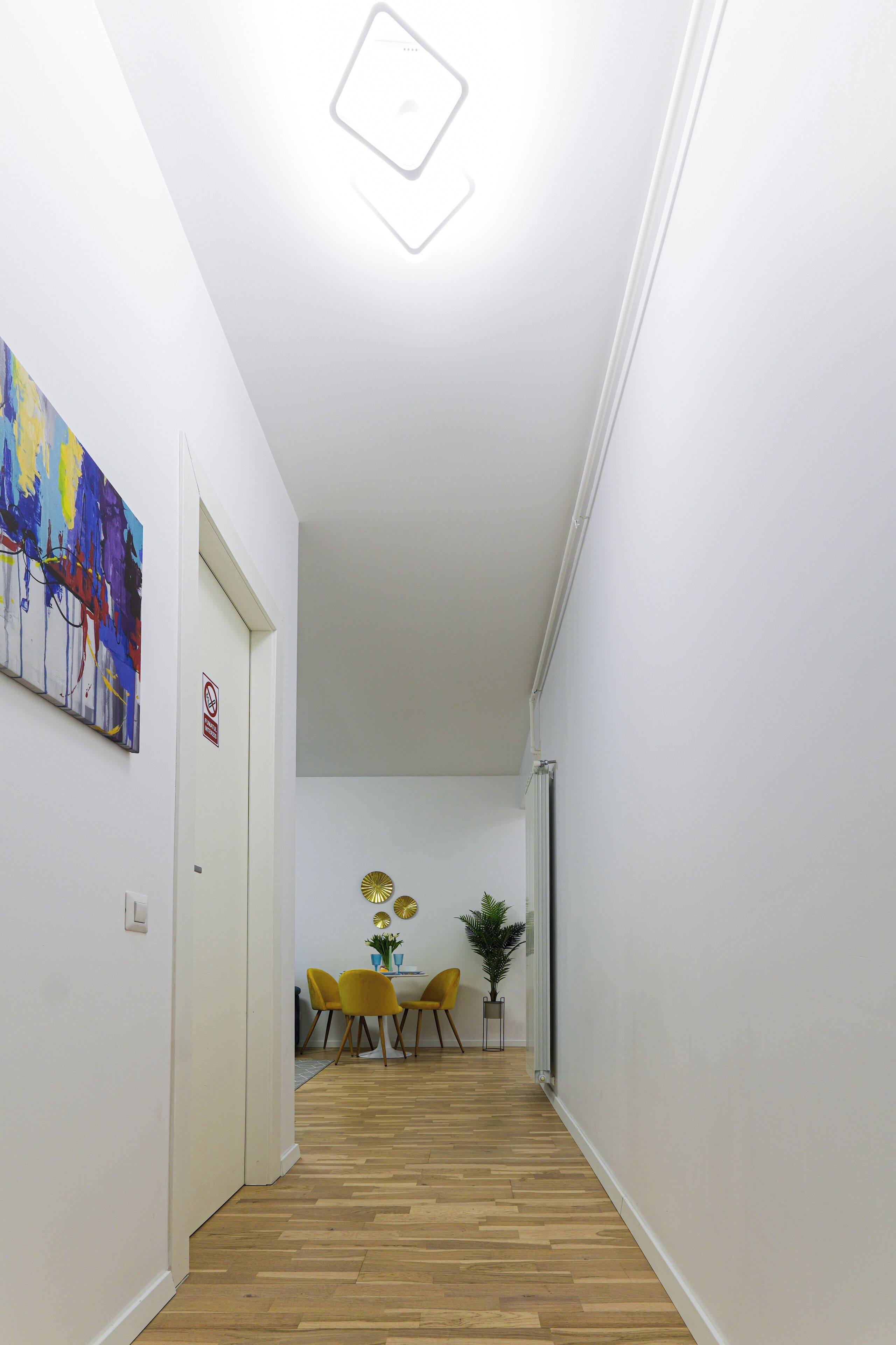 Un couloir avec un plancher en bois, un coin repas avec des chaises jaunes et un tableau accroché au mur.