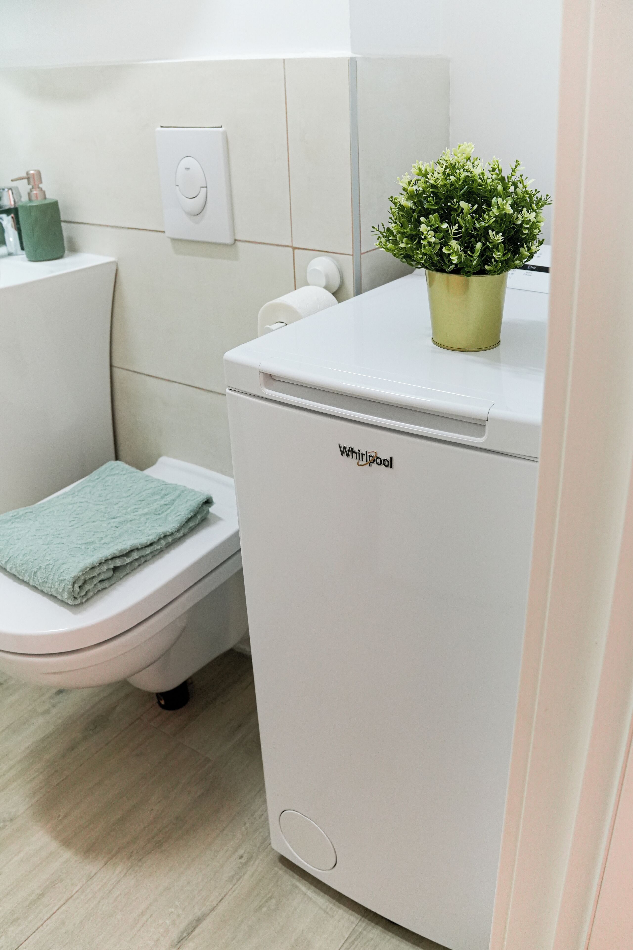 Un baño pequeño y moderno con inodoro, una lavadora Whirlpool blanca y una planta verde encima de la lavadora.