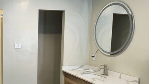 A bathroom with a white sink, wooden vanity, and a mirror with a circular frame. - Exclusivo Inn by OYO Grand Prairie, TX (Grand Prairie)