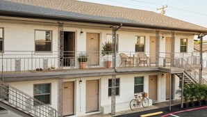 A two-story motel with a balcony, potted plants, and a bicycle parked outside. - Exclusivo Inn by OYO Grand Prairie, TX (Grand Prairie)
