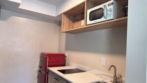 A compact kitchen with a red refrigerator, a microwave on a wooden shelf, and a sink with a faucet. - Exclusivo Inn by OYO Grand Prairie, TX (Grand Prairie)