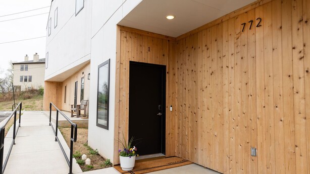 Ein modernes Gebäude mit Holzfassade, einer schwarzen Tür und der Hausnummer 772.