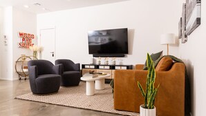 Ein modernes Wohnzimmer mit Flachbildfernseher, zwei Sesseln, einer Couch und einem Couchtisch.