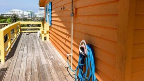Une terrasse en bois avec un tuyau d’arrosage et un robinet, une rambarde et un bâtiment doté d’un toit en pente.
