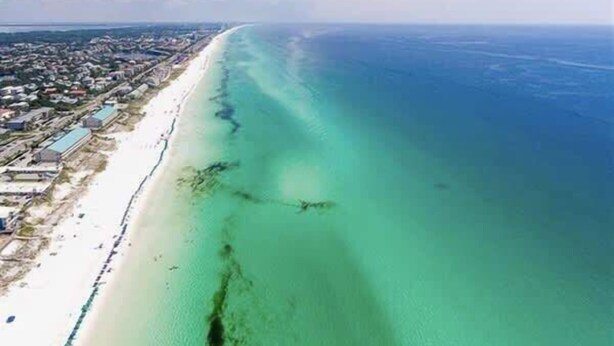 An aerial view of a coastal area with a long stretch of beach and a clear blue sea.