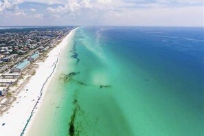 An aerial view of a coastal area with a long stretch of beach and a clear blue sea.