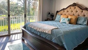A bedroom with a large bed, a balcony, and a view of greenery.