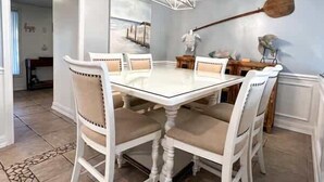 A dining area with a white table and chairs, a hanging light fixture, and a painting on the wall.