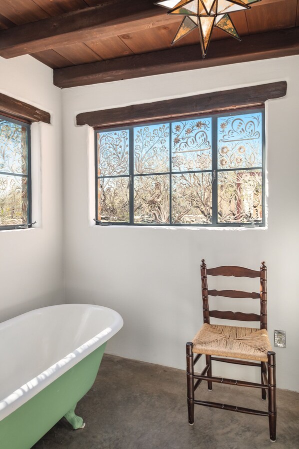 A bathroom with a freestanding bathtub, a wooden chair, and a decorative window with floral patterns.