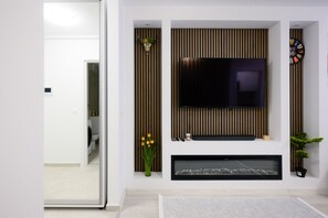 A modern living room with a flat-screen TV mounted on a wooden panel wall, a framed picture below, and a small plant to the right. - CHARMING HIDEAWAY BY EL PROFESOR'S INTRIGUE (București)