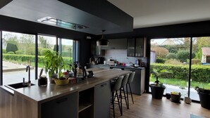 A modern kitchen with a large island, bar stools, and potted plants. - Villa Oriel 1 à Neufchâtel-hardelot Avec Piscine (Neufchâtel-Hardelot)
