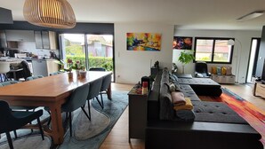 A modern living room with a dining area, a sofa, a TV, and a kitchen in the background. - Villa Oriel 1 à Neufchâtel-hardelot Avec Piscine (Neufchâtel-Hardelot)