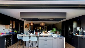 A modern kitchen with a central island, bar stools, and built-in appliances. - Villa Oriel 1 à Neufchâtel-hardelot Avec Piscine (Neufchâtel-Hardelot)