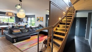 A modern living room with a staircase, a sofa, a rug, and a dining area. - Villa Oriel 1 à Neufchâtel-hardelot Avec Piscine (Neufchâtel-Hardelot)