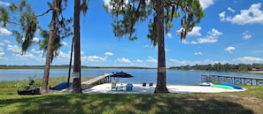 A lakeside deck with chairs and a table, surrounded by trees and a dock extending into the water.