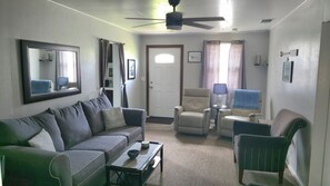 A living room with a sofa, armchairs, a coffee table, a ceiling fan, and a door with a window.