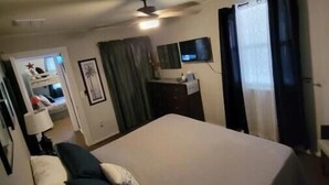 Ein Hotelzimmer mit Bett, Schreibtisch, Fernseher und Deckenventilator.