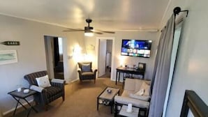 Ein Wohnzimmer mit einer Couch, Sesseln, einem Couchtisch, einem Fernseher und einem Deckenventilator.