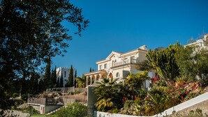 A large, multi-story building with a white facade and arched windows, surrounded by lush greenery and a clear blue sky. - Malagasuite Villa Moriana (Mijas Pueblo)