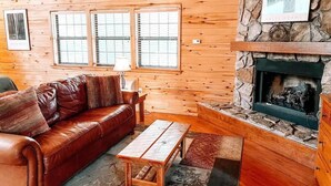 A cozy cabin interior with a leather sofa, a wooden table, and a stone fireplace. - Secluded Escape | Spacious Deck (Ruidoso)