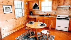 A wooden cabin interior with a dining table, chairs, a kitchen with wooden cabinets, a stove, and a hanging light fixture. - Secluded Escape | Spacious Deck (Ruidoso)