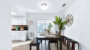 A dining area with a dark wooden table set for four, a potted plant, and a wall-mounted compass decoration. - Private Pool + NEW Luxury Hot Tub | 15 Min Beach (Bradenton)