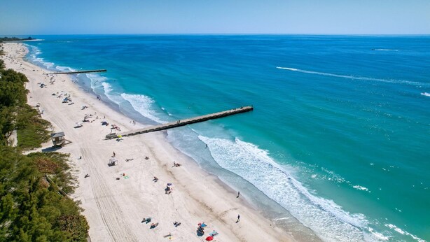 An aerial view of a beach with a wooden pier extending into the ocean, sandy beach, and clear blue water. - Private Pool + NEW Luxury Hot Tub | 15 Min Beach (Bradenton)