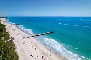 An aerial view of a beach with a wooden pier extending into the ocean, sandy beach, and clear blue water. - Private Pool + NEW Luxury Hot Tub | 15 Min Beach (Bradenton)