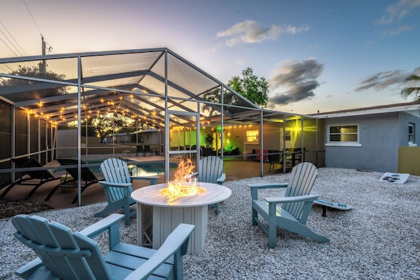 A covered outdoor seating area with Adirondack chairs, a fire pit, and a pool.