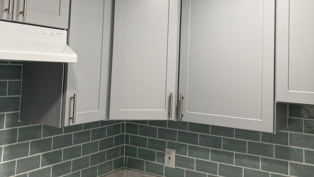 Una cocina con gabinetes blancos, encimera blanca y azulejos de protector contra salpicaduras color turquesa.