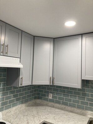 Cozinha com armários brancos, bancada branca e azulejos de parede verde-água.