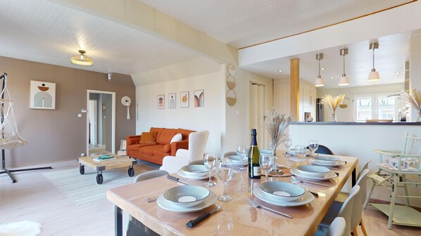 A spacious dining area with a long table set for six, a sofa, and a kitchen area with modern appliances.