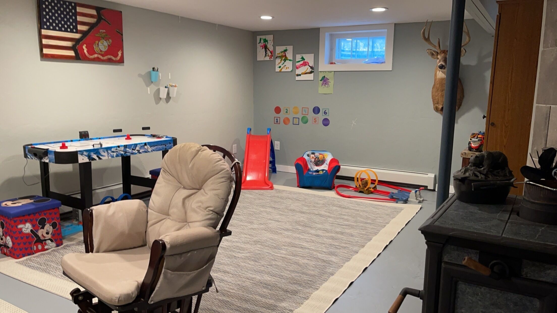 A room with a foosball table, a bean bag chair, a play area with a slide, and a wall with educational posters.