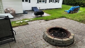 Une terrasse dotée d’un foyer en pierre, de mobilier d’extérieur et d’un espace barbecue couvert.