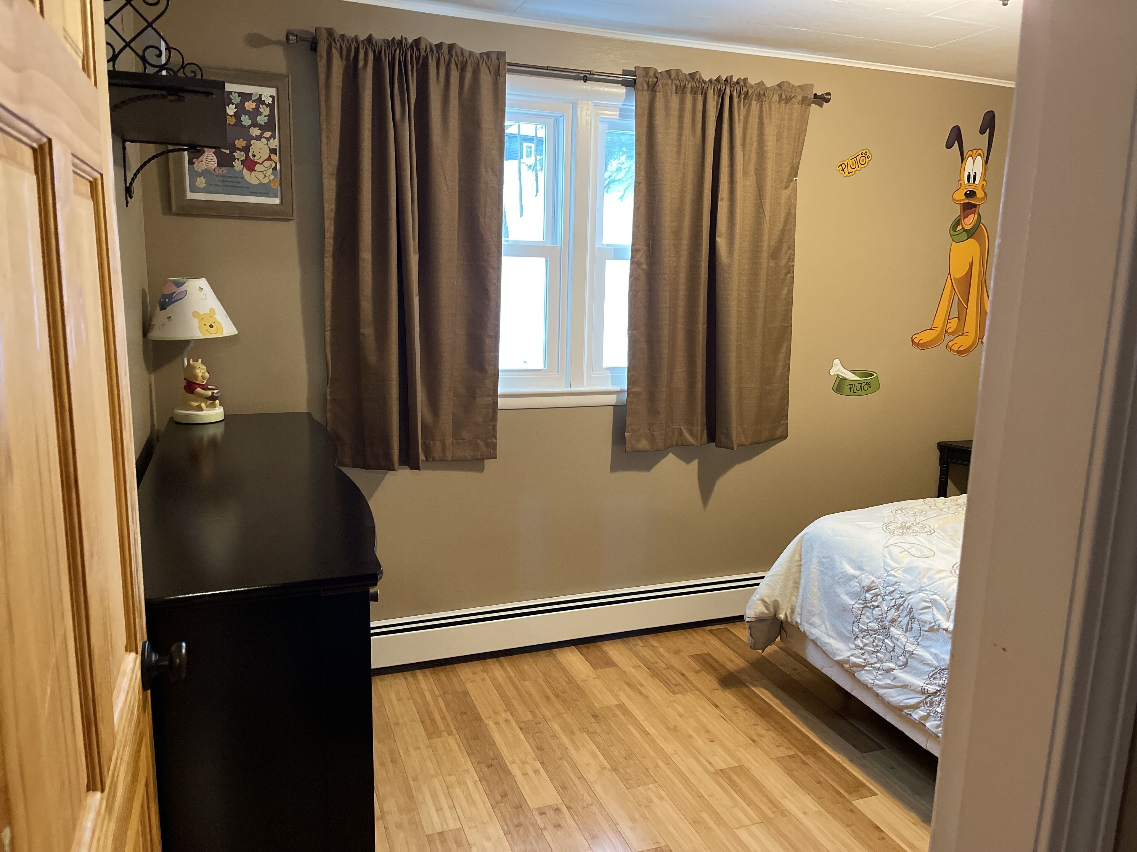 A bedroom with a window, curtains, a bed, a lamp, and a wall decoration.