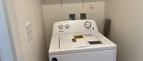 Lavadora y secadora apilables, de color blanco, con panel de control para nivel de agua y temperatura de lavado, y una pequeña etiqueta de instrucciones en la puerta.