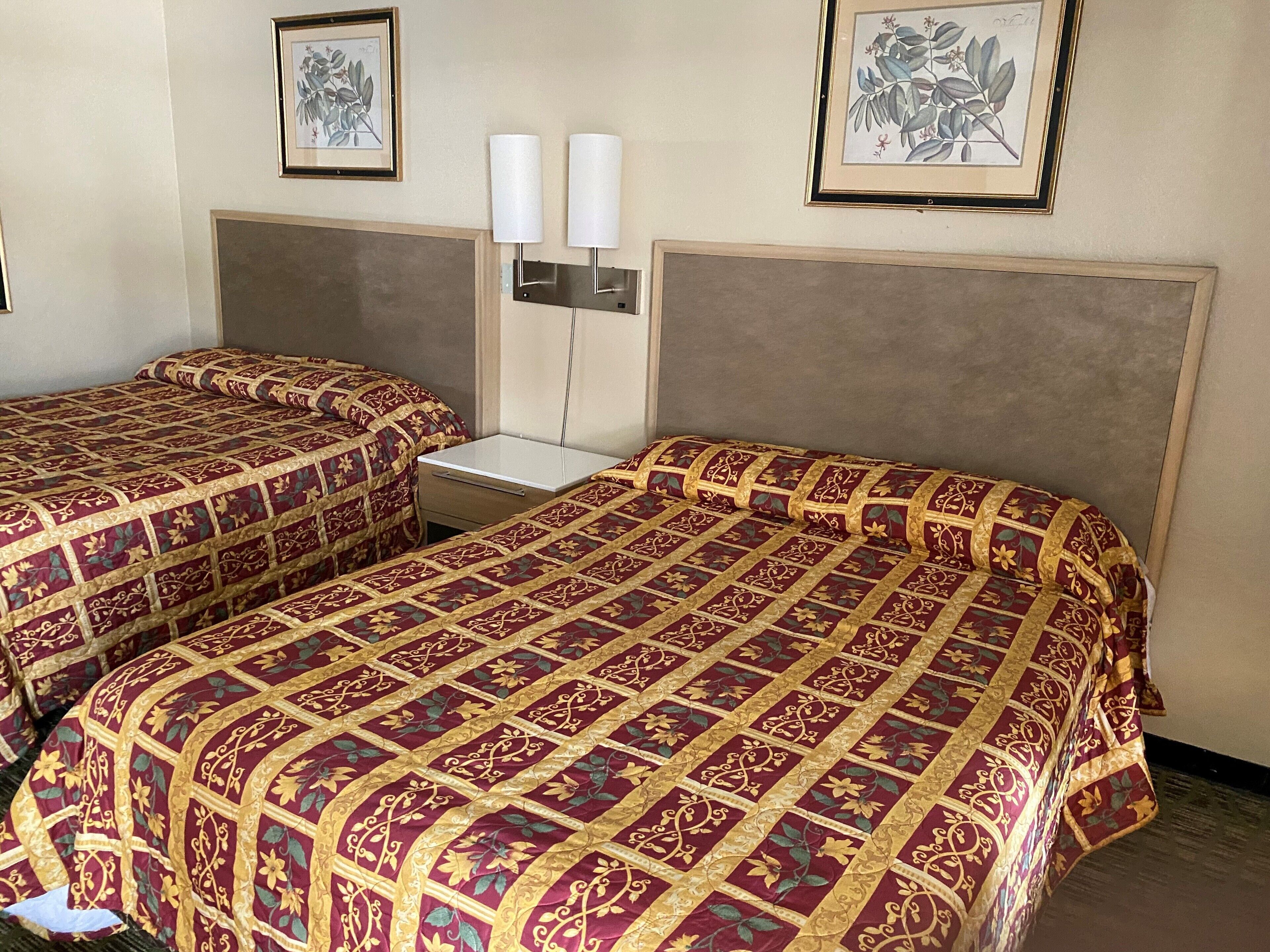 Habitación de hotel con dos camas, cada una con una colcha estampada, una mesita de noche y lámparas de pared.