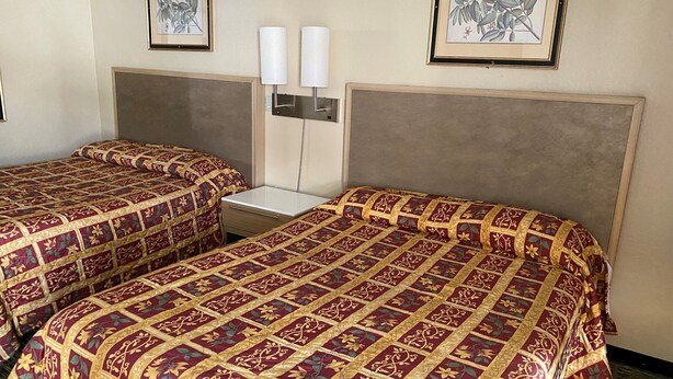 Habitación de hotel con dos camas, cada una con una colcha estampada, una mesita de noche y lámparas de pared.