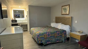 Un dormitorio con cama, mesita de noche y un escritorio pequeño con silla. Hay un espejo sobre el escritorio y un cuadro en la pared.