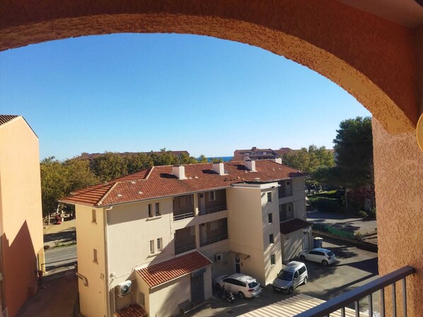 A residential building with a tiled roof, multiple balconies, and a parking area with cars.