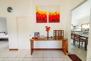 A modern living room with a wooden coffee table, two abstract paintings, a clock, and a dining area visible through an open door. - Sleeps up to 8 , additional 6 dollars fee over 8 bungalow house. (Tagbilaran)