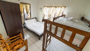 Ein Zimmer mit zwei hölzernen Betten, einem Holzstuhl und einem Fenster mit Vorhängen.