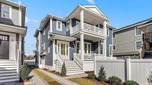 Ein zweistöckiges Haus mit einer Veranda, einer Treppe, die zum zweiten Stock führt, und einem weißen Zaun, der das Grundstück umgibt.