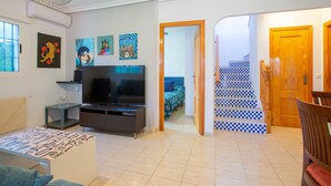 Un salon avec un téléviseur, des œuvres d’art accrochées au mur, un escalier et une porte en bois.